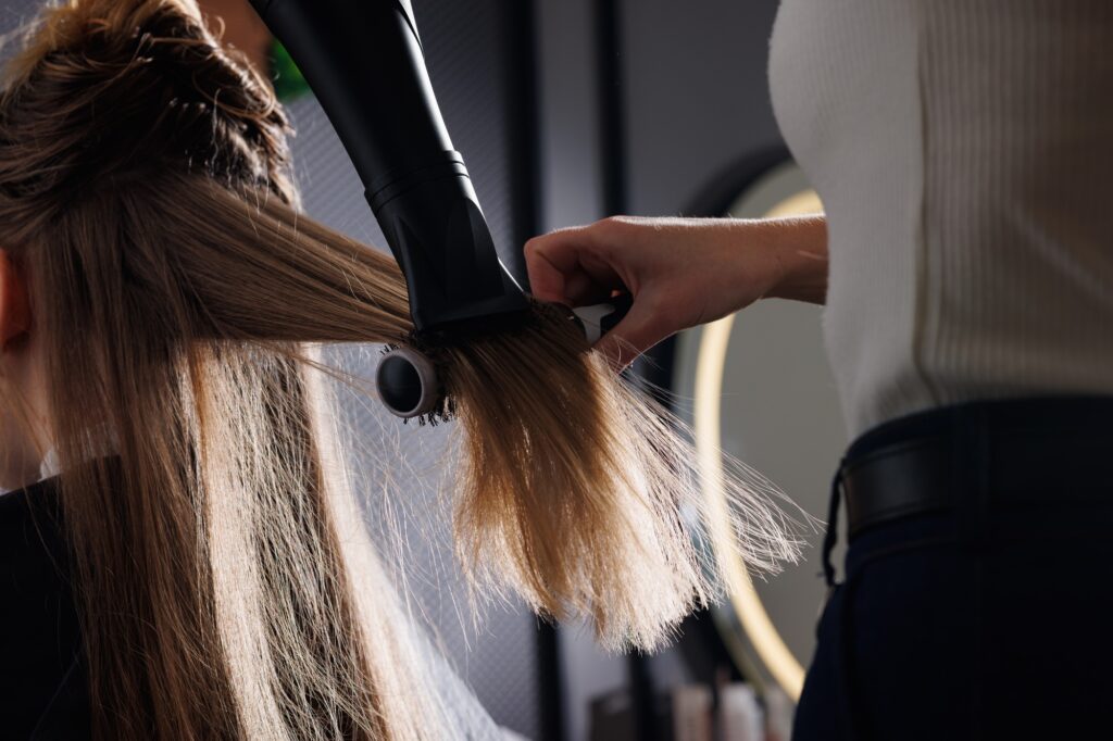 hairdresser blow-drying hair with a comb in a beauty salon, blow-drying hair close-up